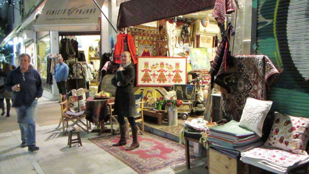 A vendor stands outside of a shop at the market.